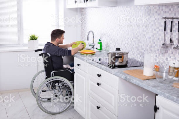 Man in wheelchair doing dishes over kitchen sink